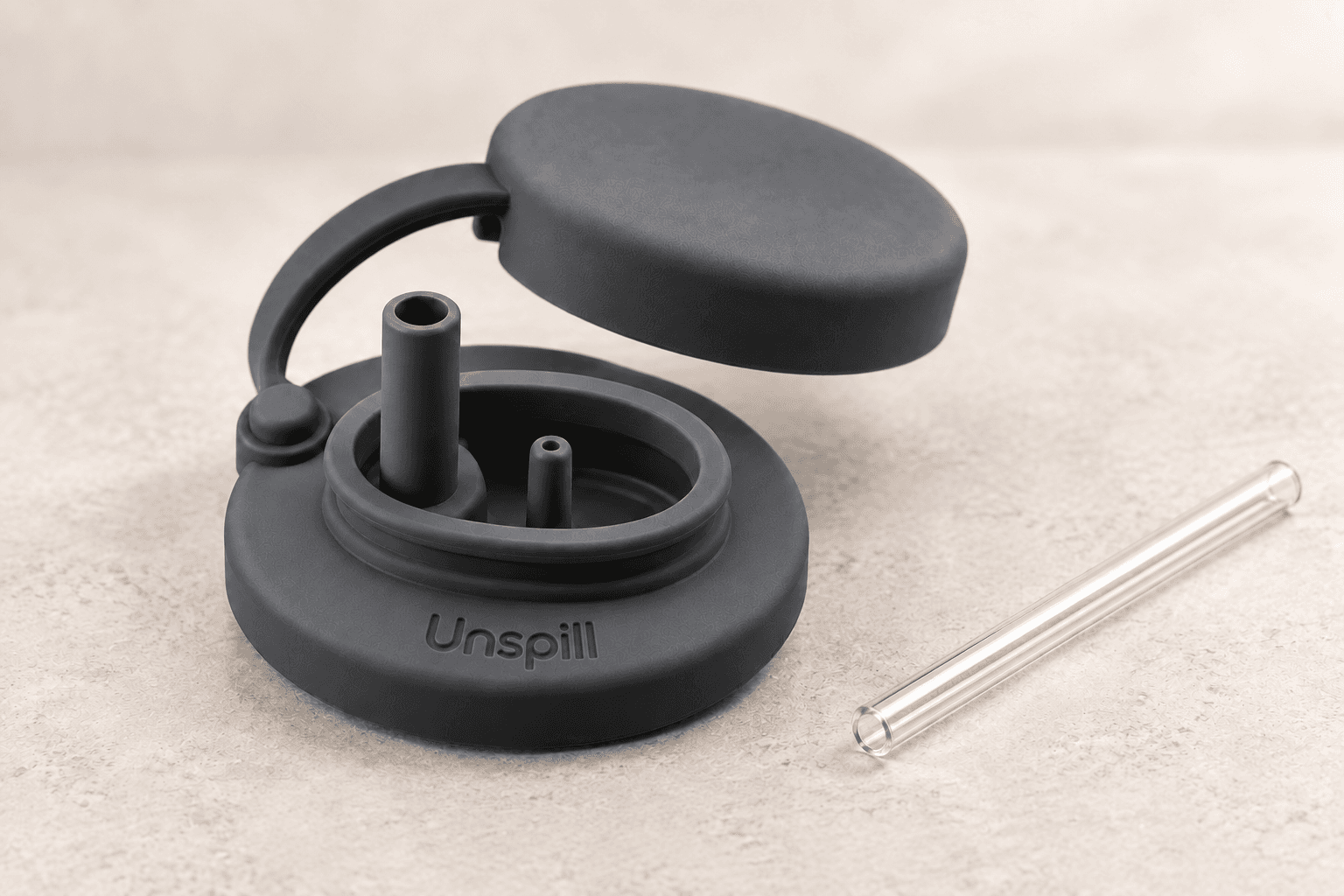 Charcoal Unspill can cover with the included transparent reusable straw resting beside it